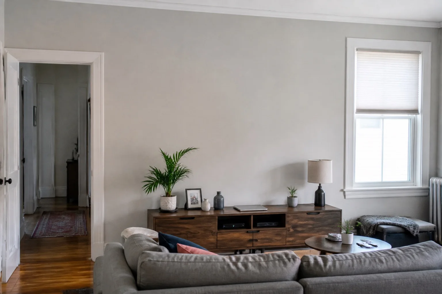 Original sample living room with neutral walls, a gray sofa and wooden sideboard